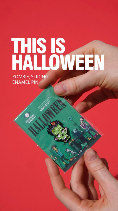 Hands holding Halloween-themed zombie sliding enamel pin packaging against a red background.