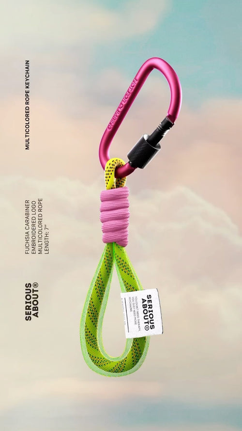 Multicolored rope keychain with a pink carabiner clip against a soft sky background.