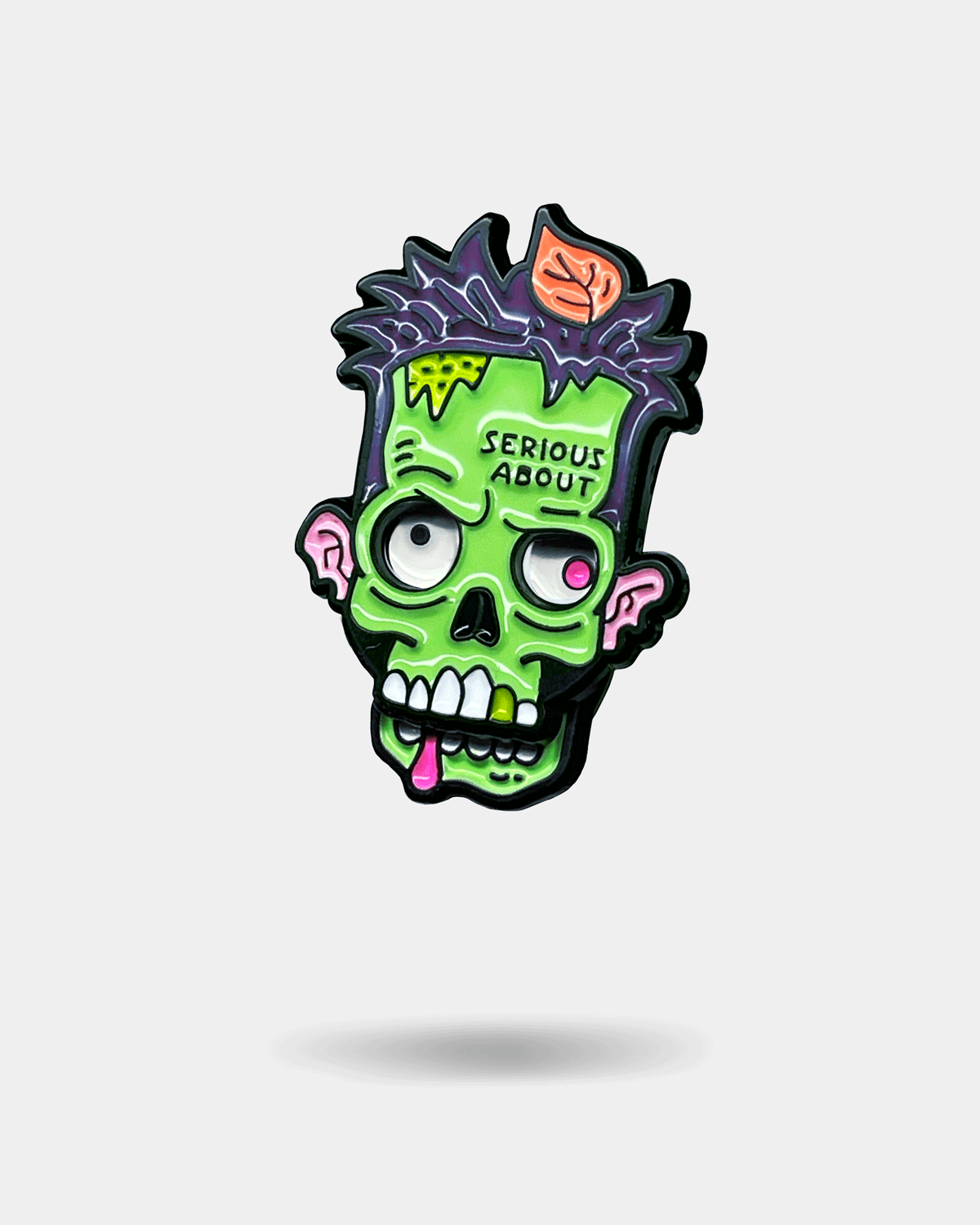 Cartoon-style green zombie head enamel pin featuring exposed brain details and bold graphic accents.